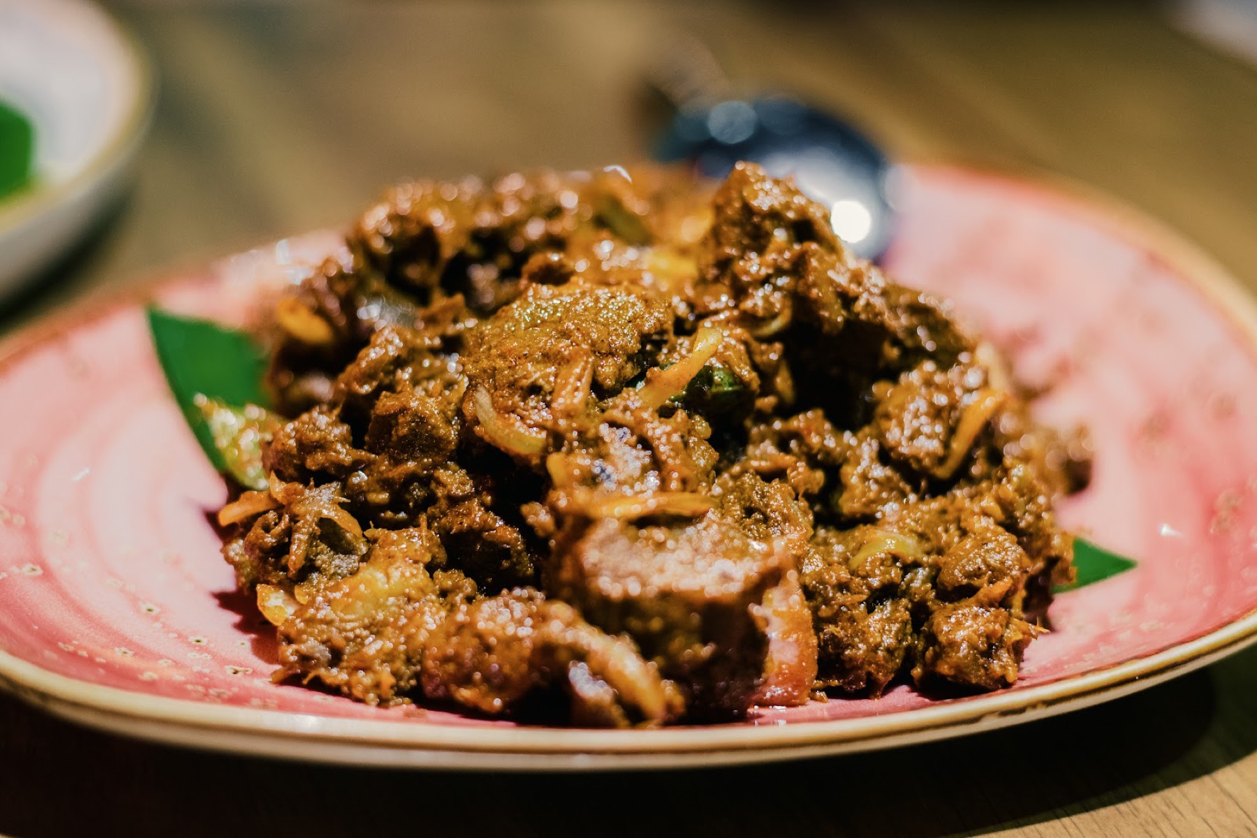 A plate of slow-fired boneless mutton varuval, spotlit against a dark table at Fire By Shankar